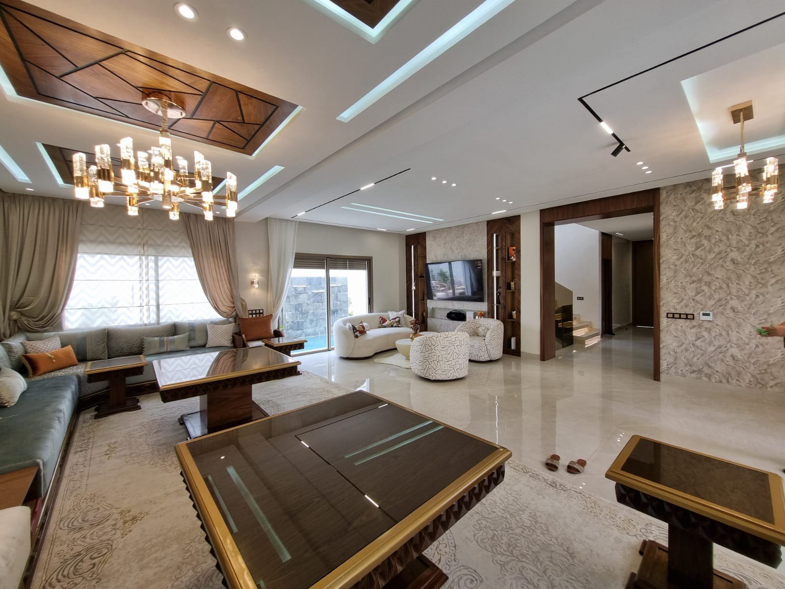 Grand séjour de villa aux tons beige et bois avec éclairage architectural